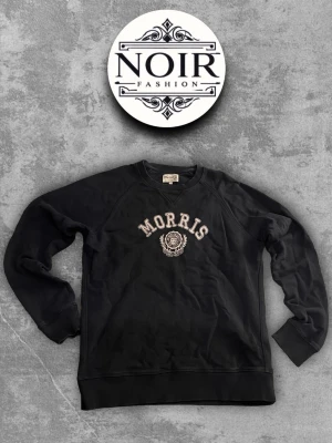 Svart sweatshirt från Morris - Svart sweatshirt från Morris med broderad logga och text på bröstet. Klassisk rund halsringning och ribbade muddar vid ärmslut och nederkant. Perfekt för en avslappnad och stilren look.