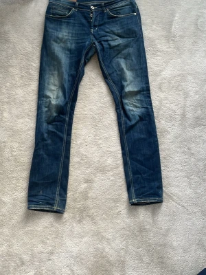 Dondup george jeans med slitningar i skrevet - Säljer ett par mörkblå jeans med raka ben och snygga slitningar på knä och ficka. Jeansen har klassisk femficksdesign, kontrastsömmar och en cool tvättad look. Perfekta för dig som gillar en avslappnad och trendig stil.