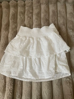 Vit volangkjol från Sernholt - Supersöt vit kjol från Sernholt med broderade hål och volanger. Kjolen har bred resår i midjan och är perfekt för sommarens alla tillfällen. Lätt och luftig i bomull med fina detaljer som ger en romantisk vibe.