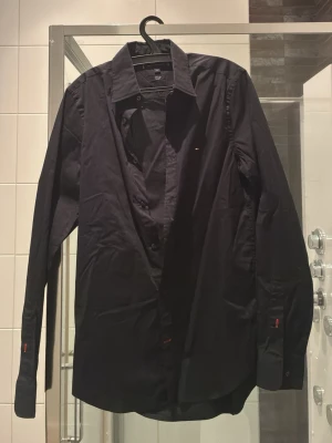 Svart slim fit skjorta Tommy Hilfiger - Snygg svart skjorta från Tommy Hilfiger i modellen THFlex Slim Fit. Skjortan har klassisk krage, långa ärmar och knappar framtill. Perfekt för dig som gillar en stilren och modern look.