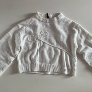 Vit stickad tröja - Säljer en vit stickad tröja med rosett motiv från H&M Divited i storlek M. Tröjan kan kännas cropped eftersom den är ganska kort, iallafall på mig. 