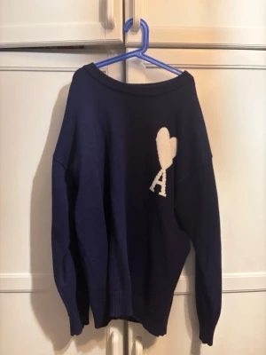 Ami Paris Tröja - Mysig mörkblå stickad tröja med en vit hjärtformad detalj och bokstaven A på bröstet. Tröjan har avslappnad passform, rund halsringning och långa ärmar. Perfekt för dig som gillar stilrena plagg med en söt twist.