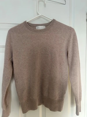 Beige cashmere-tröja från Sayless - Superskön beige stickad tröja från Sayless i mjuk cashmere. Klassisk rund halsringning och långa ärmar med ribbade muddar vid ärmslut och nederkant. Perfekt för dig som gillar stilrena och mysiga plagg.