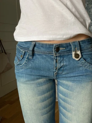 Ljusblå low waist jeans med fickdetaljer - Säljer ett par ljusblå low waist jeans med snygga slitningar och markerade sömmar. Jeansen har dubbla knappar fram, fem fickor och coola fickdetaljer bak. Köpte dessa på Vinted och nu vill sälja vidare. Jättebra skick helt nya. Priset kan diskuteras 