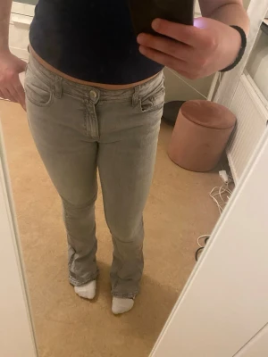 Ljusgrå bootcut jeans - Säljer ett par ljusgrå bootcut jeans med klassisk femficksdesign och normalhög midja. Jeansen har en snygg, enkel look och är perfekta för dig som gillar en avslappnad men ändå trendig stil. Materialet känns mjukt och stretchigt för extra komfort. Storlek 158 men motsvarar XS.