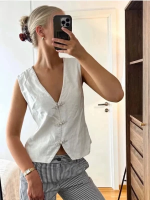 Vit linneväst med knytknappar - Säljer min så fina väst som INTE går att få tag på längre! I vitt linne med djup v-ringning och dekorativa knappar framtill. Strlk 34 och från NA-KD. Lägger ut igen för fri frakt