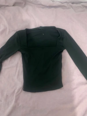 Svart långärmad topp med fyrkantig ringning - Snygg svart långärmad topp med fyrkantig ringning och figurnära passform. Perfekt att styla med jeans eller kjol för en trendig look. Tidlös design som passar till många olika outfits.
