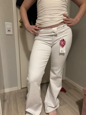 Vita bootcut jeans från Gina Tricot - Säljer ett par vita bootcut jeans från Gina Tricot. Jeansen har klassisk femficksmodell, hällor för skärp och en snygg utsvängd passform. Materialet är stretchigt och bekvämt, perfekt för dig som vill ha både stil och komfort.