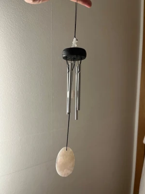 Woodstock mini vindspel med rosenkvarts  - Säljer ett stilrent vindspel med fyra silverfärgade metallrör, svart trädetalj upptill och en oval, vit snäcka längst ner. Hängs upp med svart snöre och ger ett lugnt ljud när det blåser. Perfekt som dekoration i fönster eller på balkongen.