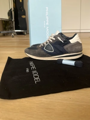 Philippe Model blåa sneakers - Snygga sneakers från Philippe Model i marinblått och grått med vita detaljer. Skorna har en låg siluett, vita skosnören och en mix av mocka och textilmaterial. Kommer med originalkartong och dustbag. Perfekta för en trendig och avslappnad stil.