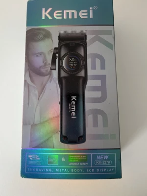 Kemei hårtrimmer KM-2279 - Elektrisk hårtrimmer från Kemei, modell KM-2279. Trimmern har svart metallkropp, LCD-display och laddas via USB. Utrustad med professionellt blad och 2000mAh batteri. Levereras i en snygg guldfärgad förpackning.