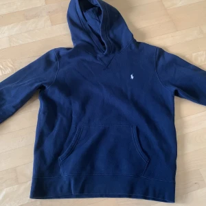 Marinblå hoodie från Polo Ralph Lauren - Säljer en marinblå hoodie från Polo Ralph Lauren i storlek XL i junior storlek. Tröjan har huva, och den klassiska broderade loggan på bröstet. passformen är normal och den är i gott skick. Passar till nästan alla kläder. Hör av dig vid frågor😃! 