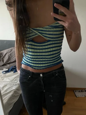 Randig ribbad tubtopp med cut-out - Stickad tubtopp i blått och ljusgrönt med ränder och en snygg cut-out detalj framtill. Toppen är axelbandslös och har en tight passform som framhäver midjan