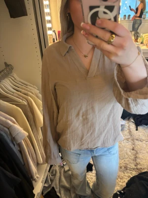 Beige linneskjorta med krage - Säljer en beige skjorta i linne med klassisk krage och v-ringning. Skjortan har långa ärmar och en avslappnad passform, perfekt för en chill och stilren look. Passar bra till jeans eller kjol.