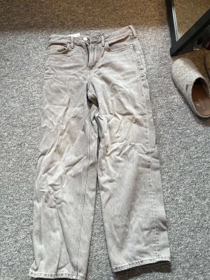 Grå loose fit jeans - Säljer ett par grå loose fit jeans från H&M med raka ben och klassisk femficksmodell. Jeansen är tillverkade i bomull och har en avslappnad passform som ger en cool och trendig look. Perfekta för dig som gillar en bekväm och stilren stil.