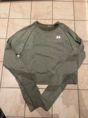 Grön långärmad träningströja - Snygg grön långärmad träningströja från lager 157 med rund hals och diskret mönster på ärmar och sidor. Tillverkad i ett stretchigt funktionsmaterial som andas, perfekt för gymmet eller löprundan. Logga i vitt på bröstet.