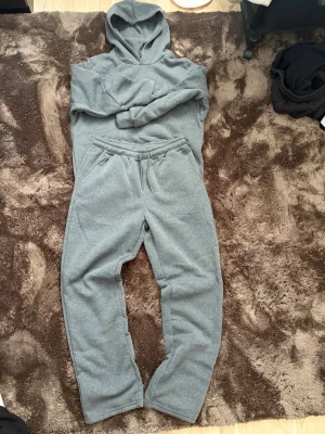 Oanvända mjukisset  - Säljer ett grått mjukisset med matchande hoodie och byxor. Hoodien har luva och långa ärmar, byxorna har dragsko i midjan och sidofickor. Väldigt skön material. Säljer dem för att dem passade inte mig