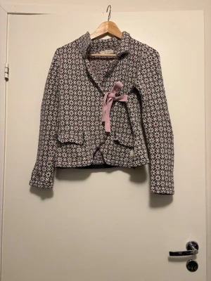 Mönstrad stickad kofta Odd Molly - Säljer en snygg stickad kofta från Odd Molly med svart, rosa och vit mönsterstickning. Koftan har en feminin passform, krage och knyts med ett rosa band i sidan. Perfekt för dig som gillar unika detaljer och mjuka material.
