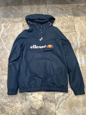 vindjacka Ellesse - Snygg mörkblå vindjacka från Ellesse med huva och stor magficka med logga framtill. Storlek Medium 