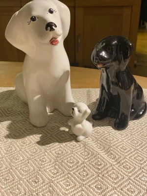 Keramikhundar i olika storlekar - Tre dekorativa hundfigurer i keramik, en stor vit, en mellanstor svart och en liten vit. Alla har blanka ytor och söta detaljer som målade ögon och nos. Perfekta som prydnad på hyllan eller skrivbordet.