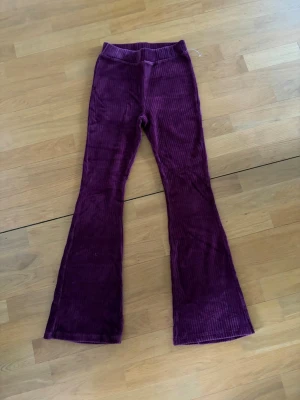 Vinröda utsvängda manchesterbyxor - Säljer ett par vinröda manchesterbyxor från KappAhl med utsvängda ben och bred resår i midjan. Byxorna har en mjuk och skön känsla tack vare det klassiska manchestertyget. Perfekta för dig som vill ha en retro och trendig look.