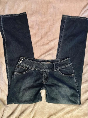 Lågmidjade bootcut jeans - Säljer ett par lågmidjade jeans✨ de är bootcut och har är jättefina med detaljen på linningen! De har blivit sydda längs med högra låret som syns på bilderna, annars i toppen-skick!  Innerbenslängd: 83cm Midjemått (rakt över): 41cm