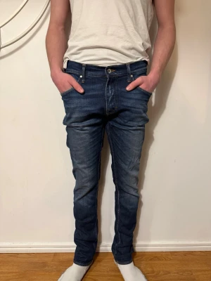 Mörkblå slim fit jeans från tiger of sweden - Snygga mörkblå slim fit jeans med klassisk femficksdesign och lätt slitna detaljer på låren. Jeansen har normal midja och smal passform hela vägen ner. Perfekta för en trendig och avslappnad look. W30 L32
