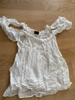 Vit offshoulder blus med volang - Säljer en söt vit offshoulder blus med volangdetaljer och rynkade kanter. Toppen har en luftig och lätt känsla, perfekt för varma dagar. Passar dig som gillar romantisk och avslappnad stil.