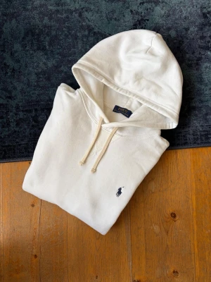 Vit hoodie från Polo Ralph Lauren - Hej!👋  Säljer en vit Ralph Lauren Hoodie mer den broderade mörkblå pony-loggan på bröstet. Hoodien är I mycket fint skick, men är lite nopprig på botten. Absolut inget som man tänker på vid användning. Storlek M. Hör av er vid frågor!💯 