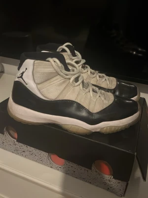 Air Jordan 11 Retro Concord Highs - Säljer ett par ikoniska Air Jordan 11 Retro Concord med svart och vit färgkombination, högt skaft och klassisk Jumpman-logga på sidan. Ovandelen är i mesh och lackat läder, med genomskinlig sula och broderad 45 på hälen. Perfekta för dig som gillar sneakers med retrovibe.
