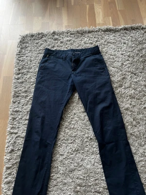 Mörkblå chinos med smal passform - Snygga mörkblå chinos med smal passform och klassisk design. Perfekta för en stilren och avslappnad look. Materialet känns mjukt och lätt, vilket gör dem bekväma att bära hela dagen. Fungerar perfekt som golfbyxor eller vanliga chinos! 