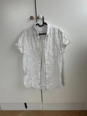 Vit kortärmad skjorta från Acne Studios  - Klassisk vit skjorta med korta ärmar och knappar framtill. Skjortan har en bröstficka och är tillverkad i mjuk bomull, perfekt för en avslappnad och stilren look. Passar till många olika outfits och är enkel att matcha. Köpt på Acne Studios i Stockholm för 2000 kr 