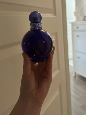 Fantasy parfymflaska lila rund - Säljer en ikonisk parfym från Britney Spears, Fantasy, i en rund lila glasflaska med silverfärgade detaljer och små kristaller. Flaskan har en matchande lila klotformad kork och ett dekorativt band runt halsen. Perfekt för dig som gillar snygga och unika parfymflaskor.