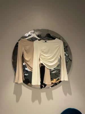 Två  långärmad topp med rynk framtill - Trendiga långärmade toppar med rynkade detaljer framtill och lätt utsvängda ärmar. Topparna har en croppad passform och är tillverkad i mjukt bomullsmaterial. Perfekt för dig som gillar en stilren men ändå unik look.