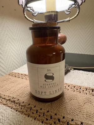 Doftljus Soft Linen i brun glasburk - Ny! Snyggt doftljus med etiketten 'Soft Linen' i en brun glasburk. Burken har en vintagekänsla och etiketten är ljus med svart text. Perfekt som inredningsdetalj för att skapa mysig stämning hemma.