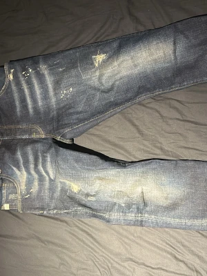 Mörkblå slitna jeans från goldgarn - Säljer ett par Goldgarn jeans med slitningar och distressed detaljer på både fram och backsida (även några färg fläckar för design) Materialet är denim och är en rakbent modell. Dem är storlek W31 i midjan och passar ungefär i längden mellan 170-178. Dem sticker ut väldigt mycket och är perfekta för en avslappnad stil, PRIS KAN DISKUTERAS!