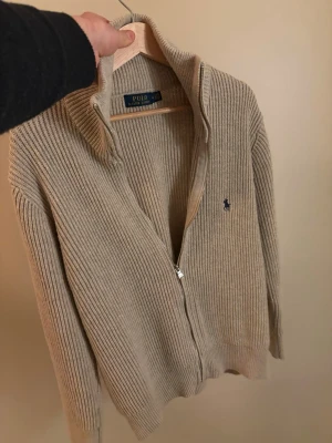 Ralph Lauren full zip cardigan  - Säljer detta sjukt feta Ralph Lauren plagget. Grymt skick, använd sparsamt 4-5 gånger. Storlek M, färg beige, sjukt snygg och stilren. Hör av er vid frågor/ fler bilder! 
