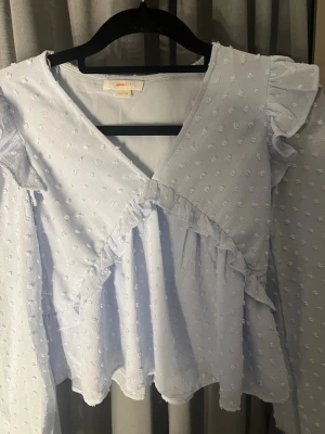 Ljusblå volangblus från Gina Tricot - Supersöt ljusblå blus med volanger och strukturprickar från Gina Tricot. Omlottmodell framtill, v-ringning och långa ärmar med volangdetaljer. Tunt, luftigt tyg som ger en romantisk känsla. Passar perfekt till sommaren☀️Är i storlek 146/152 men skulle säga att den passar xxs också.