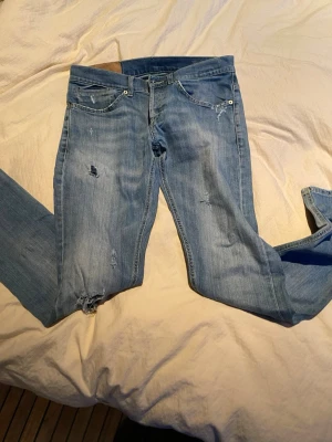  Dondup Ljusblå slitna jeans med raka ben - Säljer ett par dondup  ljusblå jeans med raka ben och slitningar på låret och knät. Jeansen har klassisk femficksdesign och är gjorda i denim med en snygg tvättad look. Perfekta för en avslappnad och trendig stil.