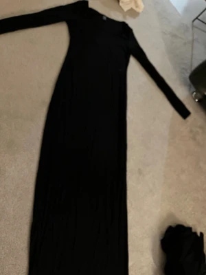 Svart långklänning med lång ärm - En elegant svart långklänning med långärmad design och figurnära passning. Perfekt för dig som vill ha en stilren och klassisk look. Klänningen har enkel form och är tillverkad i ett mjukt material som följer kroppen.