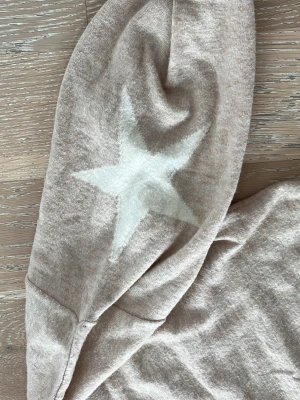 Beige stickad tröja med stjärna - Beige stickad tröja med rund hals och lång ärm. På ena ärmen finns en vit stjärna som detalj. Tröjan har en avslappnad passform och är tillverkad i mjukt material, perfekt för en chill look.