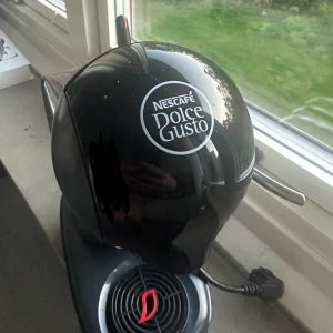 Nescafé Dolce Gusto Kaffemaskin - Snygg och kompakt Nescafé Dolce Gusto kaffemaskin i svart. Vattenbehållaren är intakt och maskinen ser ut att vara i gott skick med endast mindre ytliga repor. Perfekt för snabb och enkel bryggning av kaffe och andra drycker med kapslar.  Jag skickar även med kapslar som ingår i priset 