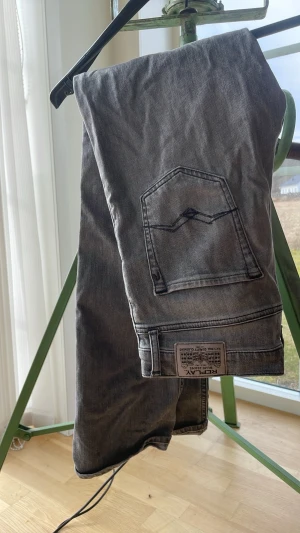 Grå raka jeans från Replay - Säljer ett par grå jeans från Replay med raka ben och klassisk sopad tvätt. Jeansen har fem fickor, tydliga sömmar och Replay-lapp bak. Perfekta för en avslappnad och sopad look.