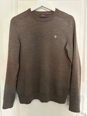 Grå stickad tröja från Morris - Snygg brun stickad tröja från Morris med rund halsringning och diskret broderad logga på bröstet. Tröjan har långa ärmar och ribbade muddar vid ärmslut och nederkant. Perfekt för en snygg stil och passar till mycket. Storlek M men Morris tröjor är lite mindre i storlek. Tveka inte med att fråga.