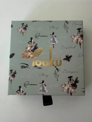 Loaku blomörhängen  - Säljer ett par unika örhängen från Ioaku i guldfärgad metall. Örhängena har en stor blomformad design med en liten glittrande sten i mitten och en tunn kedja som binder ihop två blommor. Hör av dig vid eventuella frågor!