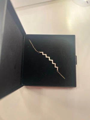 Guldigt armband med zickzack-design - Snyggt armband i guld med en unik zickzack-formad detalj. Armbandet har en tunn kedja och geometrisk design som ger en modern och trendig look. Perfekt accessoar för att lyfta din outfit.