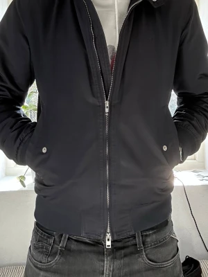 J.Lindeberg Jacka - Snygg vårjacka från J.Lindeberg med dragkedja och ribbade muddar. Jackan har två fickor med tryckknappar och klassisk krage. Perfekt för dig som vill ha en stilren och enkel look. Perfekt jacka nu när solen börjar kika fram☀️                                       Hör gärna av dig vid intresse!