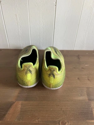  legalis gula Adidas fotbollsskor - Säljer ett par gula Adidas fotbollsskor med svarta detaljer och klassiska tre ränder på sidan. Sk mold ACHLESS design utan snörning för tight passform och bra bollkontroll, samt mesh-liknande material för lätt känsla på planen. Perfekta för dig som vill sticka ut på fotbollsplanen.