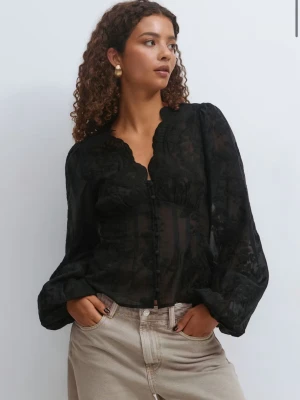 Svart transparent blus med spetsdetaljer - Svart blus med transparent tyg och vackra spetsdetaljer. Blusen har en feminin, figurnära passform, dekorativa knappar framtill och en scallop-formad v-ringning. Långa ärmar med lätt puff och diskret mönster i tyget. Perfekt för att skapa en cool och elegant look.
