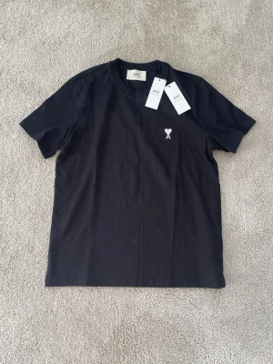 Svart t-shirt från Ami Paris - Snygg svart t-shirt från Ami Paris med deras ikoniska hjärta-A broderat på bröstet. Klassisk passform och rund halsringning. Tillverkad i mjuk bomull som känns skön mot huden. Perfekt basplagg med stilren design och diskret logga.
